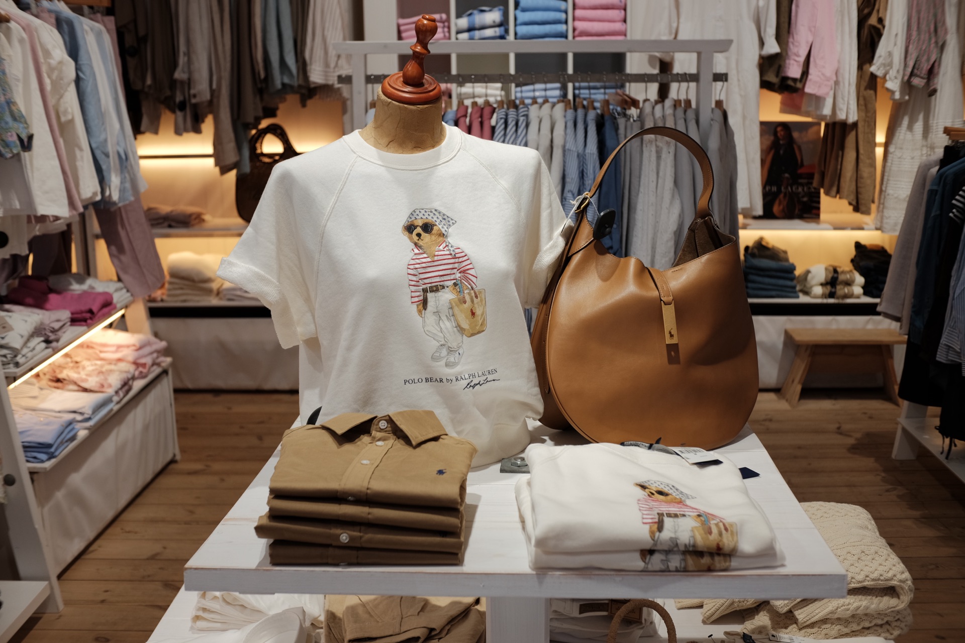 Bordet med Polo Bear-sweatshirts, stablede skjorter og en lædertaske