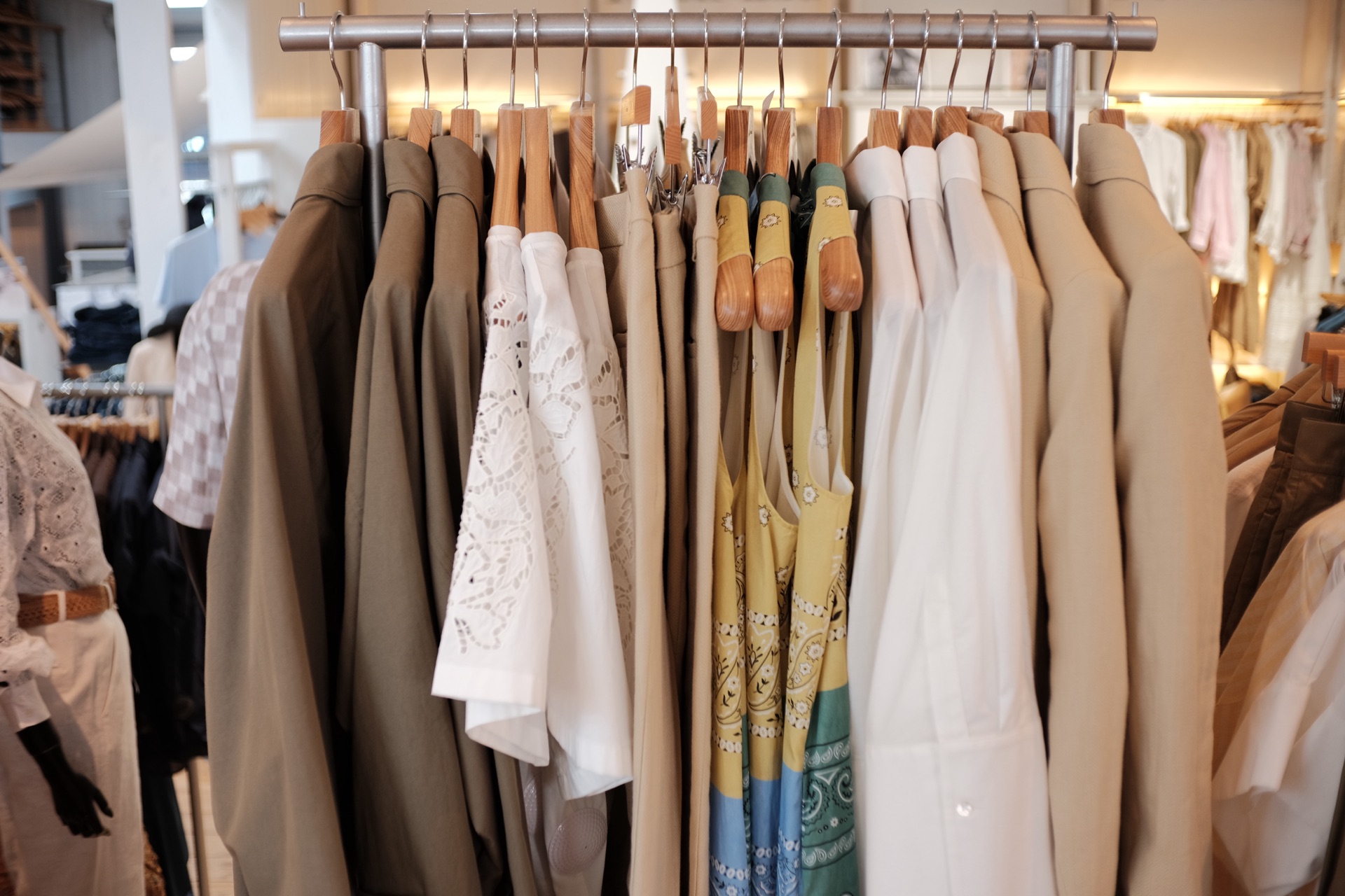 Stativ med olivengrønt overtøj, hvide broderede bluser og mønstrede kjoler